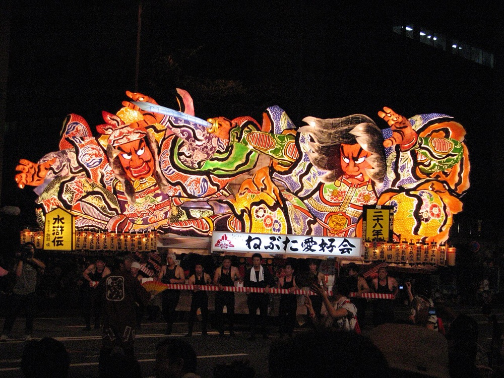 Un carro luminoso del Nebuta di Aomori avanza di notte fra la folla