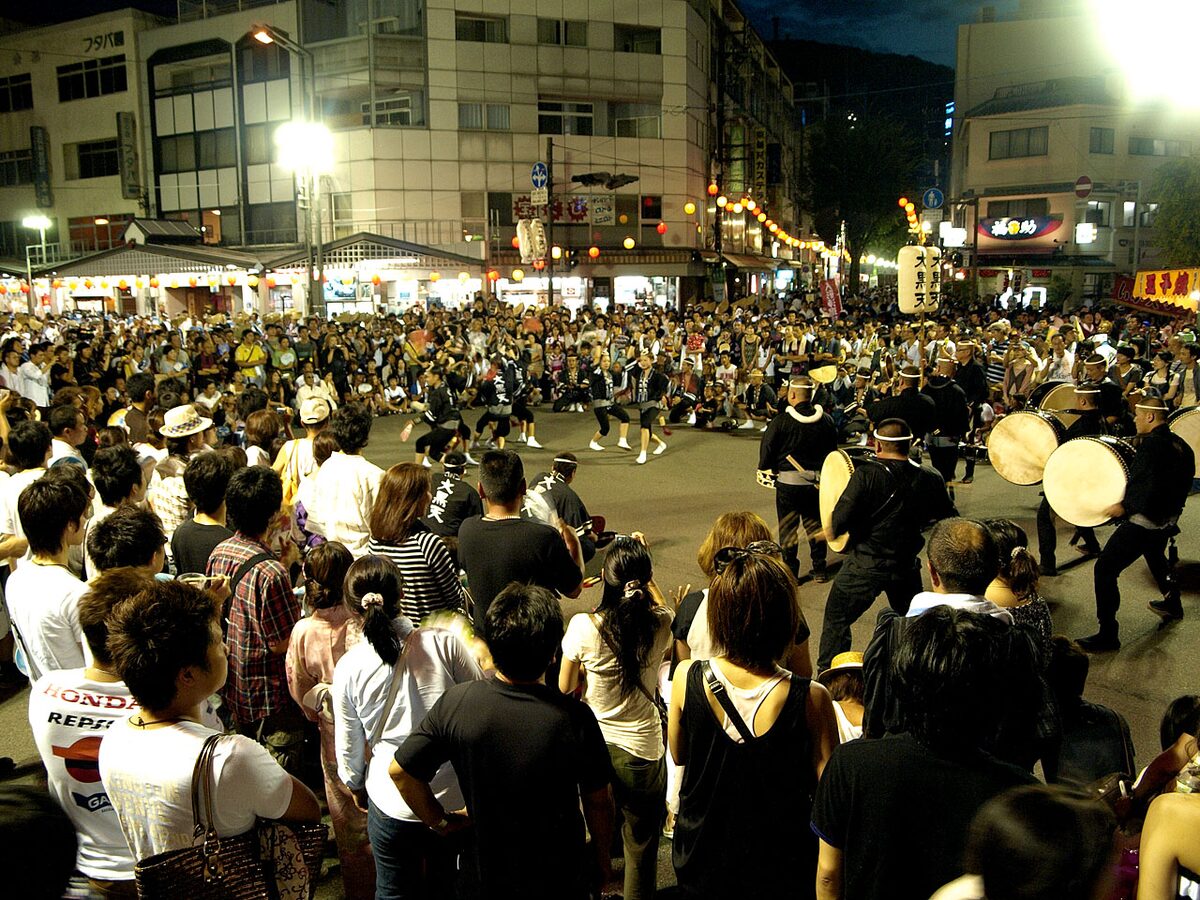 Danzatori e grandi tamburi dell’Awa Odori si esibiscono di notte in una strada di Tokushima circondata dal pubblico.