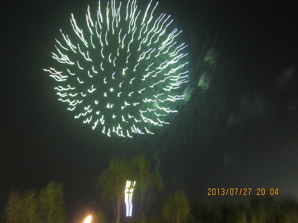 Un grande fuoco d’artificio bianco e verde si apre nel cielo notturno sopra le luci del festival.