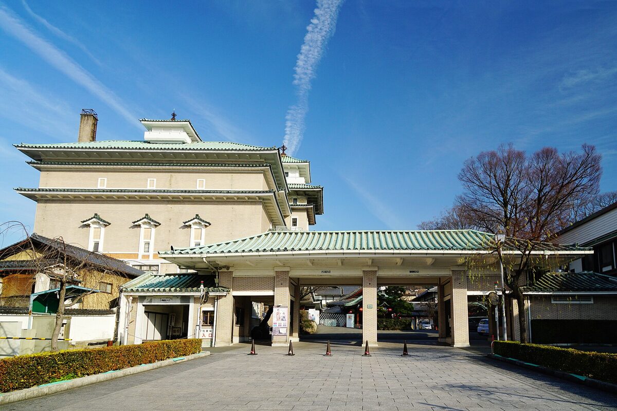 Ingresso monumentale del Gion Kobu Kaburenjō sotto un cielo blu, con tetti verdi e cortile vuoto.