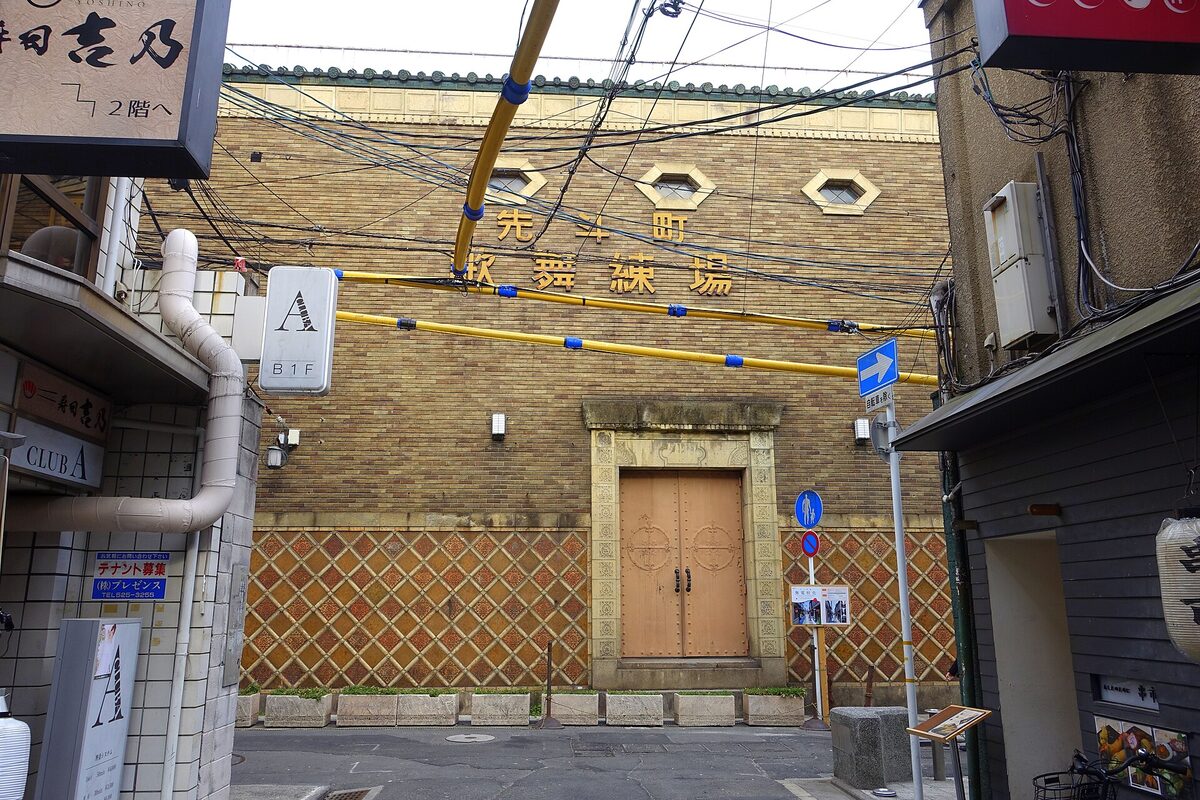 Facciata in mattoni del Pontochō Kaburenjō in fondo a un vicolo, con portone chiuso, insegne e cavi aerei.