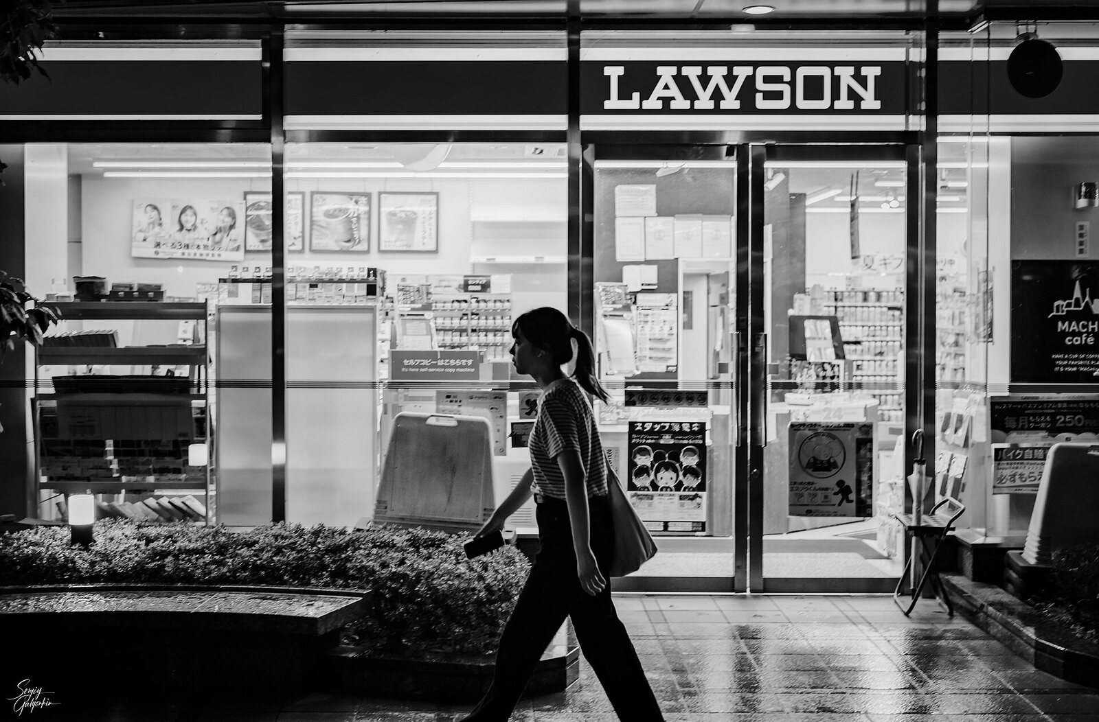 Un Lawson illuminato di notte a Sendai, visto dalla strada mentre passa una persona