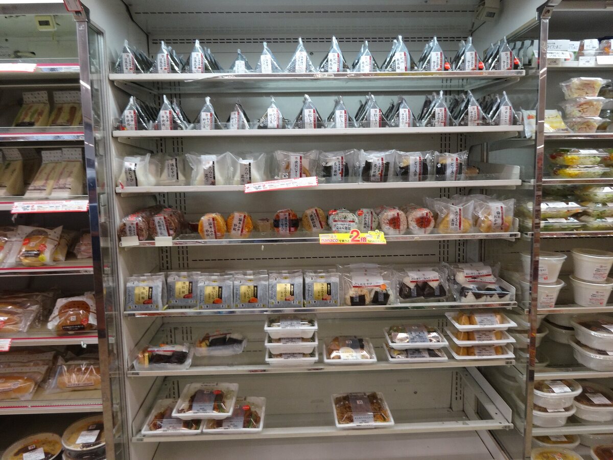 Scaffali refrigerati di un konbini con onigiri, sandwich e altri pasti pronti confezionati