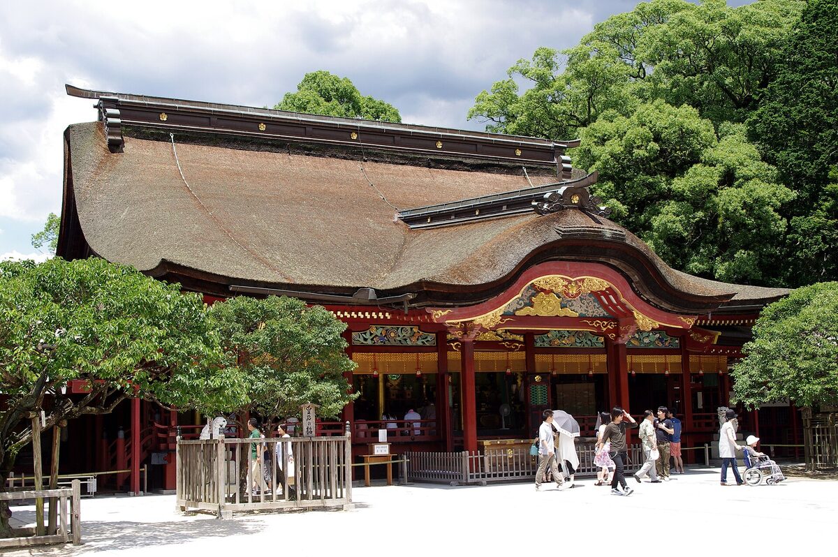 Edificio principale rosso e dorato di Dazaifu Tenmangū, con grande tetto curvo e visitatori nel cortile.