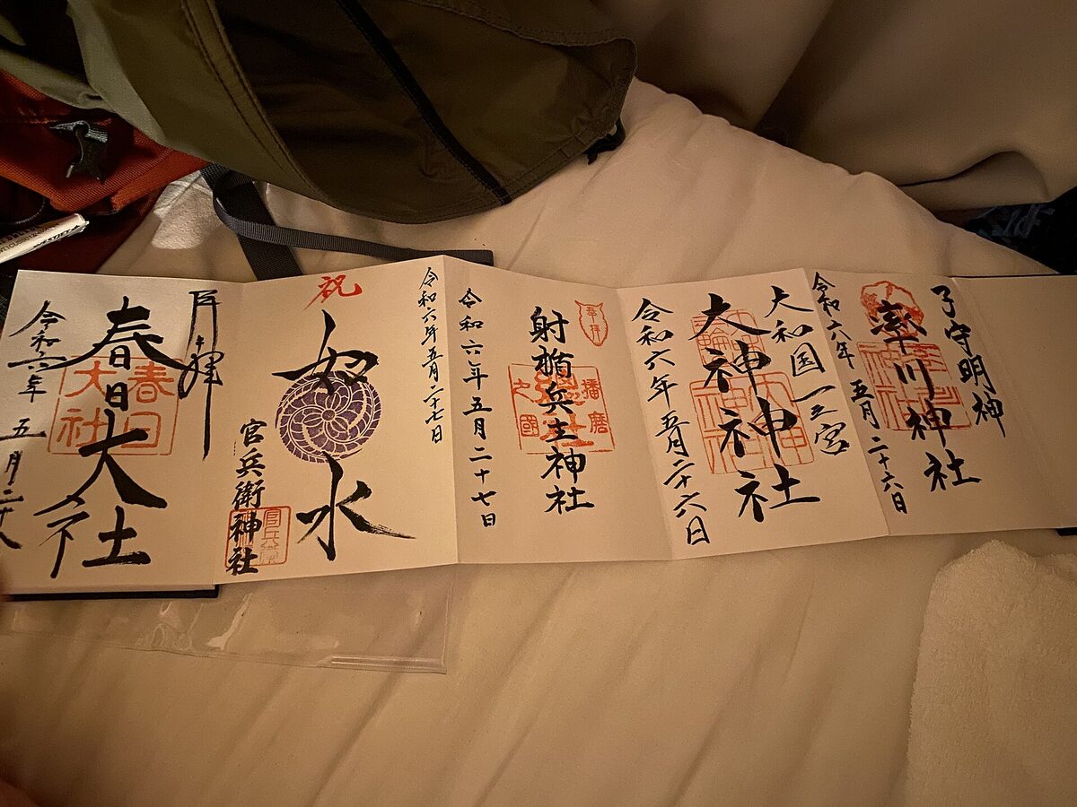 Goshuinchō aperto a fisarmonica con più calligrafie nere, date e sigilli rossi di santuari diversi.