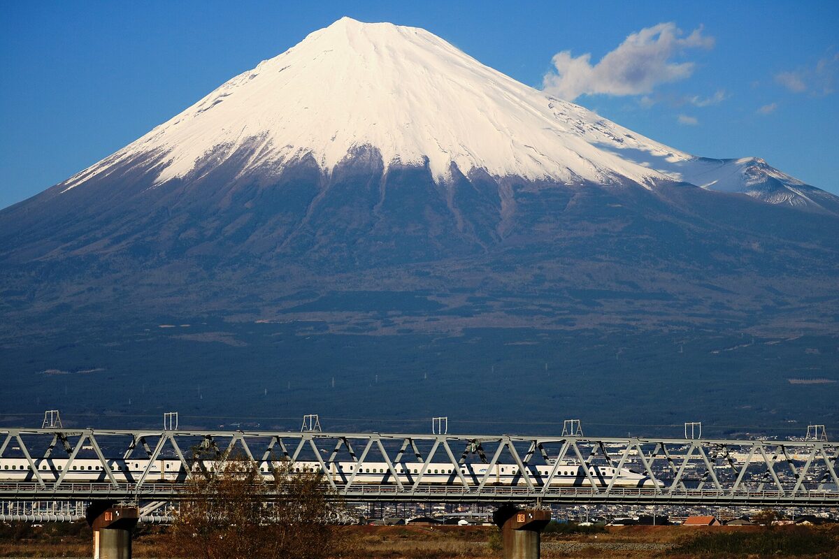 Uno Shinkansen bianco attraversa un ponte ferroviario davanti al profilo innevato del monte Fuji.